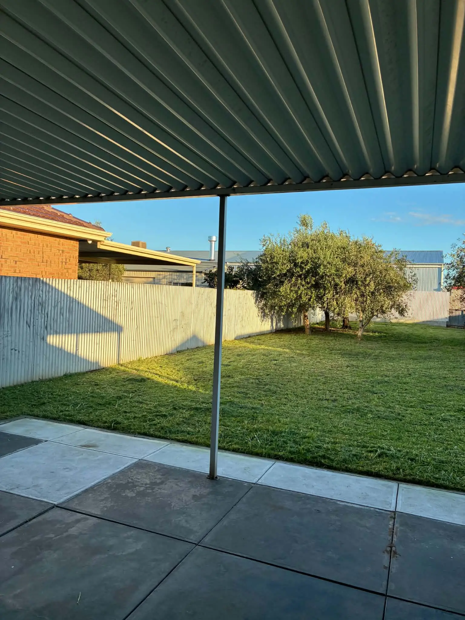 A back yard with the long grass mown short, seen from under a pergola.